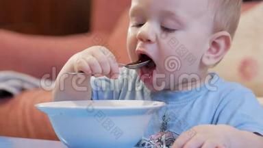 一个2岁有魅力的男孩自己在吃红汤。 勺子和手流动的液体。 健康饮食的概念